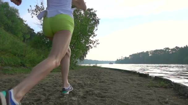 Chica brunnete delgada corriendo a orillas del río de verano arenoso. Super cámara lenta grúa de vídeo — Vídeo de stock