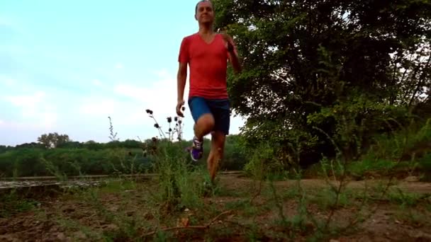 Mannelijke atleet in rode tshirt loopt langs de rivieroever. Super SlowMotion steadicam clip — Stockvideo