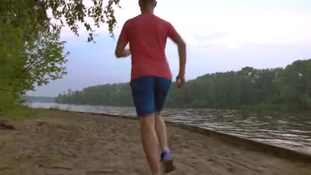 Steadicam vidéo de l'homme athlétique courant le long de la rivière sablonneuse, 4K — Video