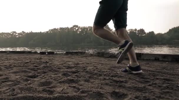 Super slow motion steadicam shot of runners legs. Sandy riverside, river and forest — Stock Video