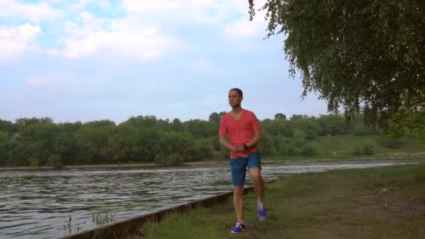 Atletische man loopt langs de zandstranden langs de rivier en cruising speedboot, 4k schot — Stockvideo