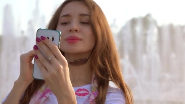 Όμορφη μελαχρινή κοπέλα σε γυαλιά ηλίου λήψης selfie με το κινητό της τηλέφωνο κοντά στο μεγάλο πάρκο fountain. βίντεο 4k — Αρχείο Βίντεο