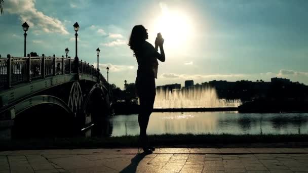 Chica delgada en gafas de sol tomando fotos de la gran fuente del parque con su teléfono celular. Vídeo 4K — Vídeos de Stock