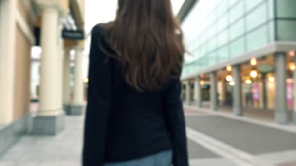 通りを歩いて彼女のショッピング バッグとジーンズでぼやけたスリム ブルネットの少女。4 k ボケ背景のビデオ — ストック動画