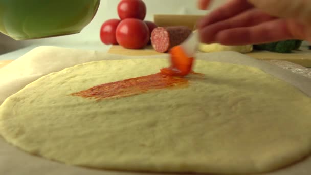 Étendre la sauce tomate sur la base de la pâte. Cuisiner des pizzas maison, ça fait partie du set. Vidéo de gros plan 4K — Video