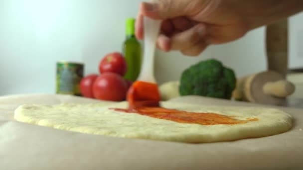 Homem espalhando molho de tomate sobre base de massa. Cozinhar pizza caseira, parte do cenário. 4K close up de vídeo — Vídeo de Stock