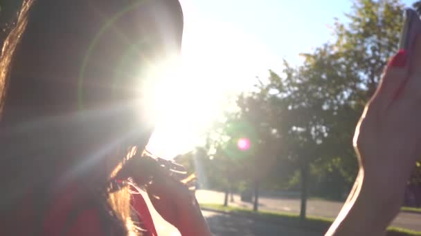 Hermosa chica morena haciendo selfie en el parque, colores cálidos atardecer. Vídeo en cámara lenta — Vídeos de Stock