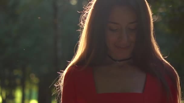 Menina morena bonita em vestido vermelho andando ao longo do beco ensolarado parque, close up. Vídeo em câmera lenta, 120 fps — Vídeo de Stock