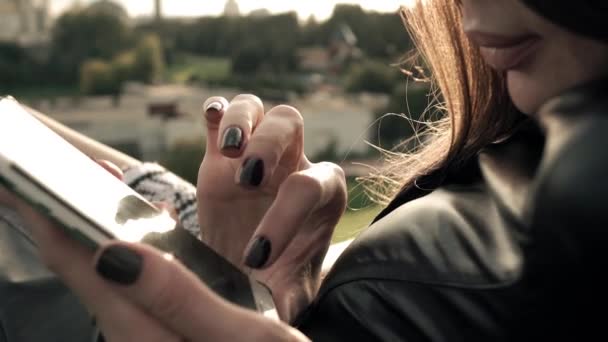 Hermosa chica morena con esmalte de uñas oscuro usando su teléfono inteligente en el parque. Tiempo libre. 4K primer plano de vídeo — Vídeo de stock