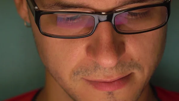 Jeune homme sérieux dans des lunettes de bord noir à l'aide de sa tablette. Écran réfléchissant dans le verre — Photo