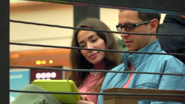 Menina morena e homem de óculos usando tablet computador juntos em um café. 4K tiro — Vídeo de Stock