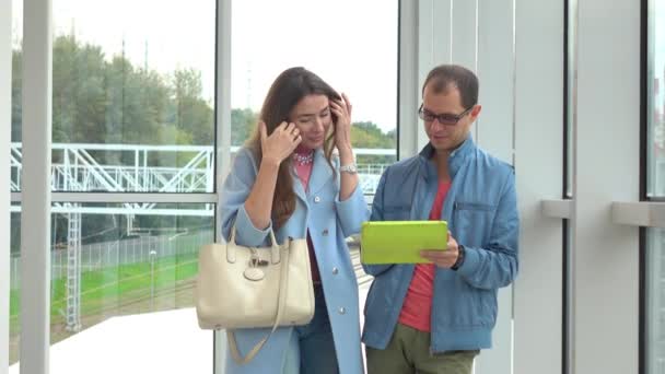 Улыбающийся мужчина и молодая женщина используют планшетный компьютер на современной железнодорожной станции. 4К выстрел — стоковое видео