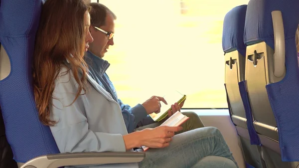 Pareja viajando en tren. Chica leyendo un libro y un hombre usando su tableta. Concepto de tecnologías antiguas versus modernas — Foto de Stock