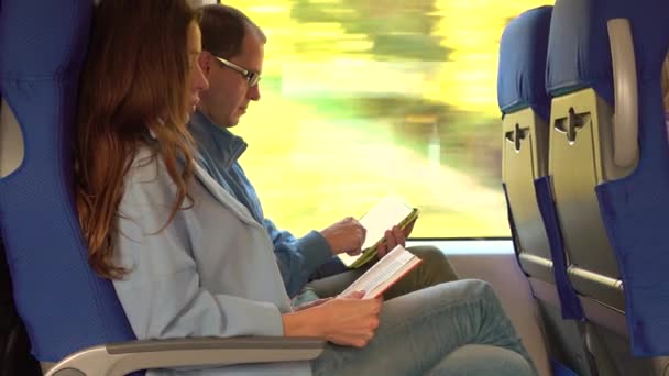 Coppia che viaggia in treno. Ragazza che legge un libro e un uomo usando il suo tablet. Concetto di tecnologie vecchie e moderne. 4K tiro — Video Stock