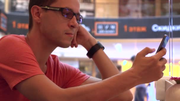 Hipster ennuyé dans des lunettes de jante noires tapant sur ses téléphones mobiles dans un café. Dépendance moderne au téléphone portable. Coup 4K — Video