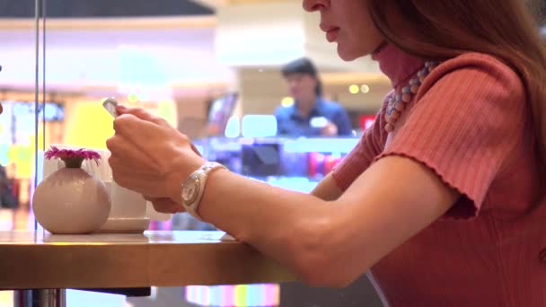 Menina morena bonita usando seu telefone celular em um café. Um vício moderno em telemóvel. 4K tiro — Vídeo de Stock