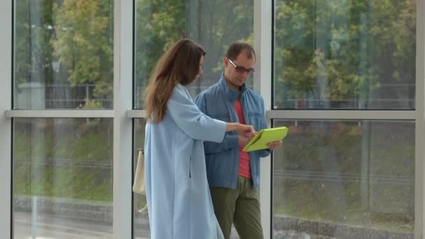 Hombre nerd y hermosa chica usando tableta cerca de la ventana grande. Disparo 4K — Vídeos de Stock