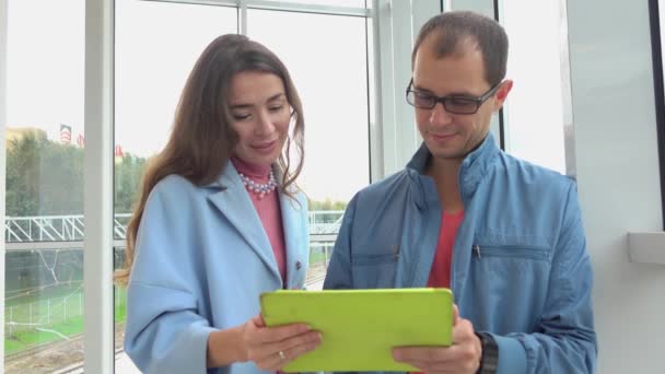 Hombre alegre y chica morena utilizando tableta en la estación de tren moderna. Clip 4K — Vídeos de Stock