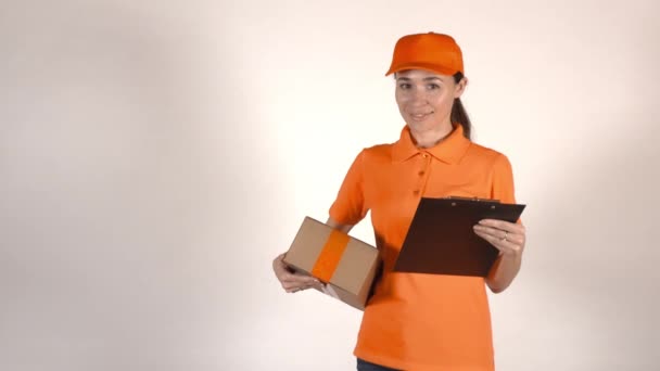 Hermosa mensajera femenina en uniforme naranja entregando un paquete. Fondo gris claro, toma de estudio 4K — Vídeos de Stock