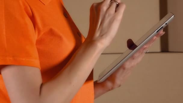 Kvindelige lagerarbejder i orange uniform bruger sin tablet computer mod brun karton stakke baggrund. 4K close up video – Stock-video