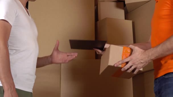 Asistente de tienda en uniforme naranja dando una caja a un cliente. Fondo de los cartones, plano de estudio 4K — Vídeo de stock