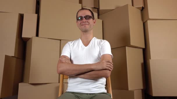 Geeky propriétaire d'une petite boutique en ligne assis contre plusieurs piles de carton. Clip 4K — Video