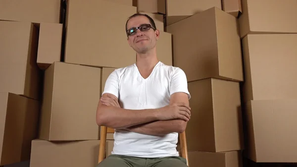 Geeky owner of small internet shop sitting against multiple carton stacks