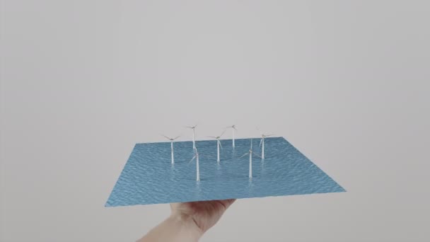 Der Mensch dreht sich in Windmühlen, die auf dem Wasser stehen. grauer Hintergrund. alternative ökologische Stromerzeugung. 4k-Clip — Stockvideo