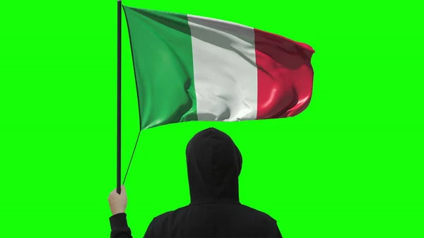 Bandiera sventolante d'Italia e uomo sconosciuto vestito di nero, isolato su sfondo verde — Foto Stock