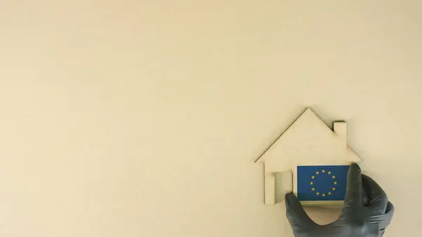 Umieszczenie tekturowej ikony domu z nadrukowaną flagą Unii Europejskiej. Koncepcja rynku nieruchomości — Zdjęcie stockowe