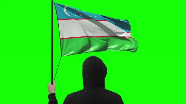 Sventolando bandiera dell'Uzbekistan e uomo sconosciuto con indosso nero, isolato su sfondo verde — Foto Stock