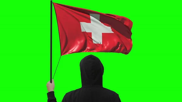 Unbekannter hält schwenkende Fahne der Schweiz auf grünem Hintergrund — Stockfoto