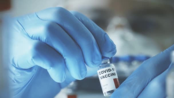 Неизвестный ученый в синих перчатках изучает флакон с вакциной COVID-19, крупным планом. — стоковое видео