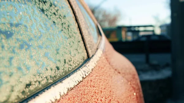 Porta e janela de um carro vermelho congelado no fundo da rua turva. Manhã fria de inverno — Fotografia de Stock