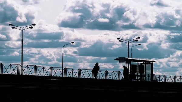 Люди на автобусной остановке и дорожном движении на фоне облаков — стоковое фото