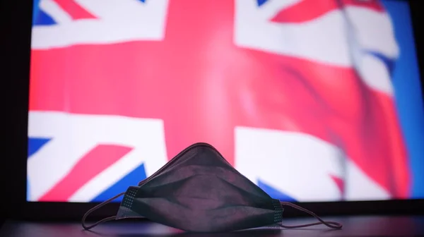 Engångs ansiktsmask mot suddig flagga i Storbritannien. Brittiskt koncept för utbrott av COVID-19 — Stockfoto