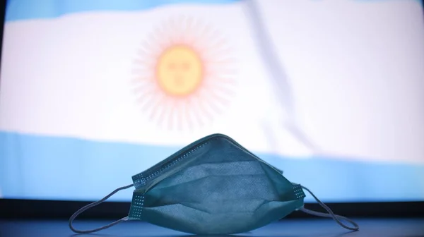 Медицинская маска против размытого флага Аргентины. Концепция вспышки COVID-19 — стоковое фото