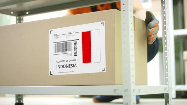 Worker takes away a carton with goods from Indonesia on the shelf — Stock Photo, Image