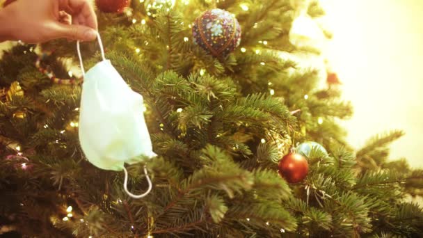 Das neue Jahr oder den Weihnachtsbaum mit einer Einweg-Gesichtsmaske schmücken. Pandemie-Zeiturlaube neues Normalkonzept — Stockvideo