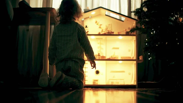 Девушка в пижаме играет с кукольным домиком дома — стоковое фото