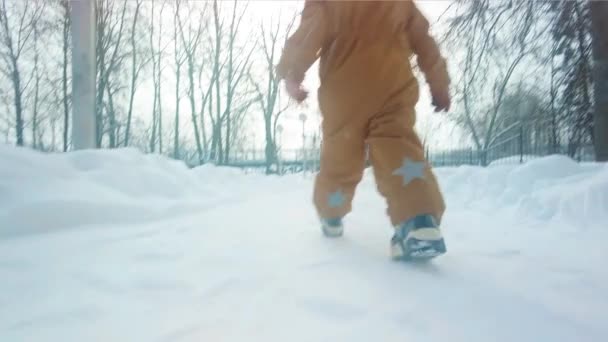 雪の公園の小道を歩くオレンジの服の少女のスローモーションショット — ストック動画