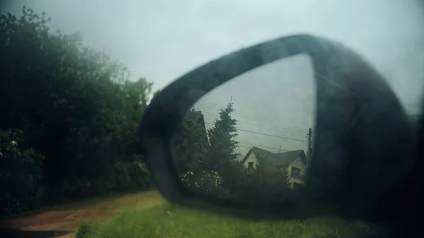 Мокрое зеркало автомобиля заднего вида отражает дом в дождливый день — стоковое фото