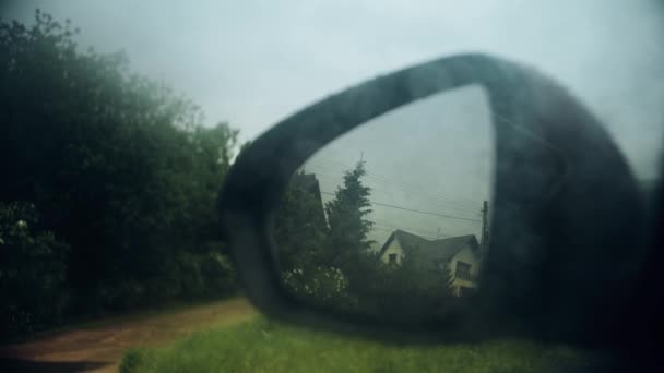 Wet rearview car mirror reflects a house on a rainy day — Stock Video