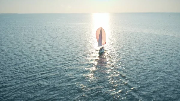 Veduta aerea di una barca a vela sconosciuta con vela rosa che si muove sul mare la sera — Foto Stock