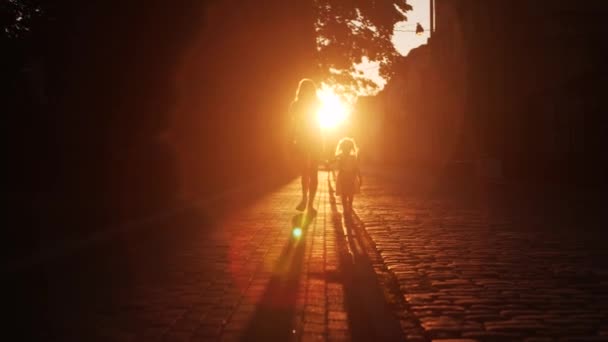 Σιλουέτα άγνωστης μαμάς και κόρης που περπατούν στο δρόμο στρωμένοι με πλακόστρωτη πέτρα το βράδυ — Αρχείο Βίντεο