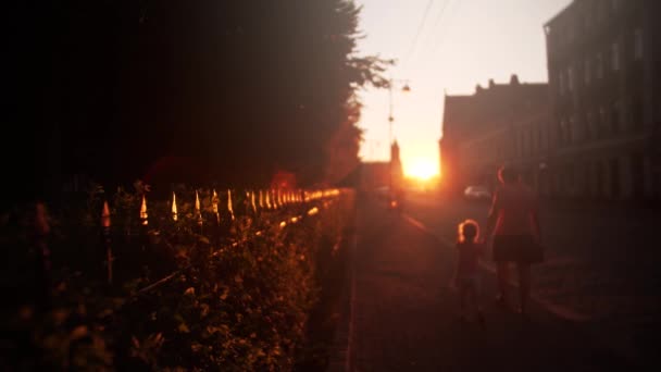 Mãe desfocada e menina caminham ao longo da rua iluminada pelo sol à noite, tiro em câmera lenta — Vídeo de Stock