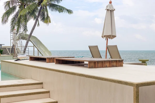 Modern şezlonglar ve çizgili sandalyeler lüks bir sonsuzluk havuzunun yanında süzülerek rahatlatıcı bir tropikal tatil atmosferi yaratırlar..