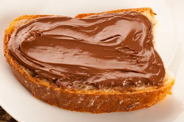 Fatia de pão com nougat de chocolate doce espalhada no prato branco — Fotografia de Stock