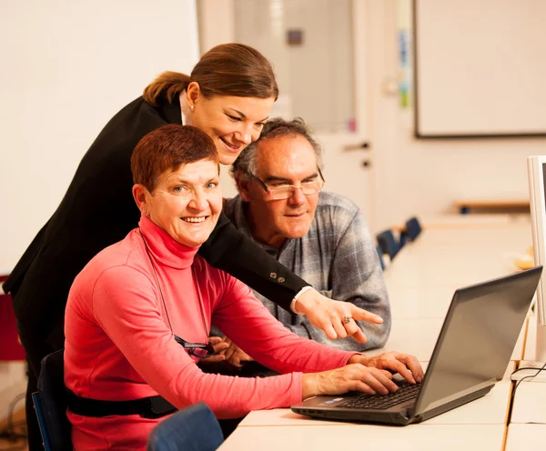 Giovane donna che insegna agli anziani coppia di competenze informatiche. Intergen — Foto Stock