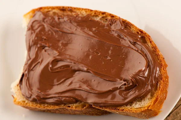 Fatia de pão com nougat de chocolate doce espalhada no prato branco — Fotografia de Stock